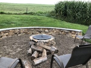 A fire pit in the middle of a field with chairs around it.